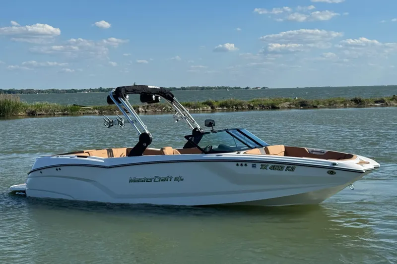 Slide: The Image of 2021 MasterCraft NXT24 boat on a serene lake under a clear blue sky. - 4