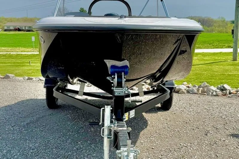 Slide: The Image of 2026 Bayliner M17 boat on trailer, parked on gravel with green landscape background. - 2