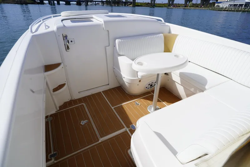Slide: The Image of 2003 Intrepid 370 Cuddy boat interior with white seating and round table on wooden deck. - 23