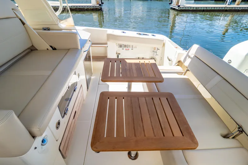 Slide: The Image of 2019 Boston Whaler 350 Realm interior with wooden tables and seating, docked by water. - 5
