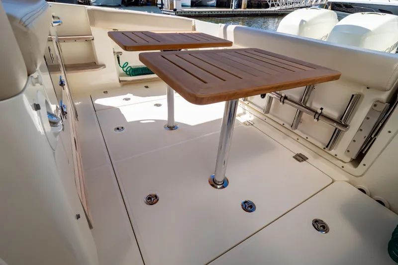 Slide: The Image of 2019 Boston Whaler 350 Realm boat deck with dual wooden tables and storage compartments. - 74