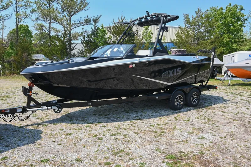 Slide: The Image of 2023 Axis T220 boat on trailer, parked outdoors, surrounded by trees and other boats. - 2