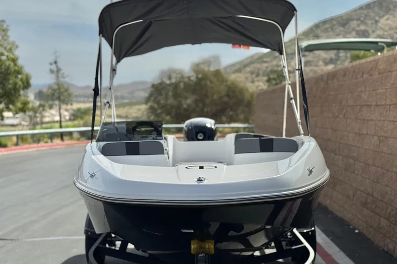 Slide: The Image of 2025 Tahoe T16 boat with canopy, parked on a scenic road with mountains in the background. - 2