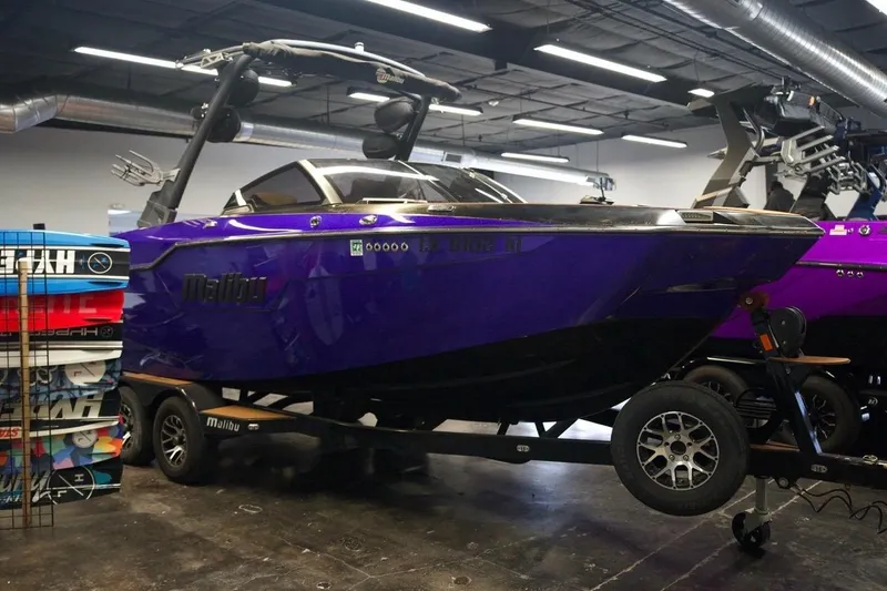 Slide: The Image of 2021 Malibu M220 boat in showroom, vibrant purple color, on trailer. - 0
