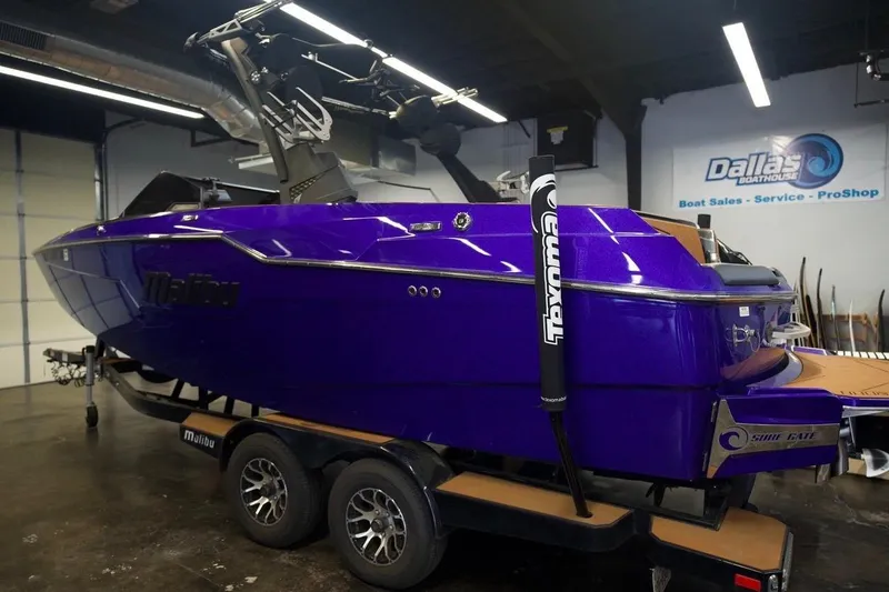Slide: The Image of 2021 Malibu M220 boat in vibrant purple on trailer at Dallas Boathouse showroom. - 1
