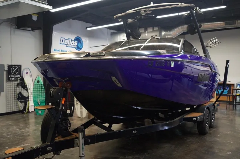 Slide: The Image of 2021 Malibu M220 boat in showroom, vibrant purple, on trailer, Dallas Boat Sales. - 2