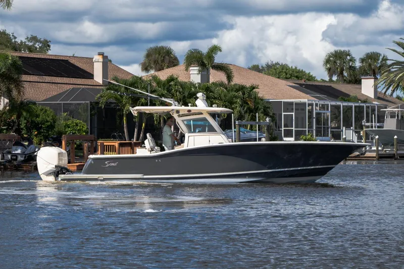 Slide: The Image of 2019 Scout 320 LXF boat cruising on a scenic waterway near waterfront homes. - 1