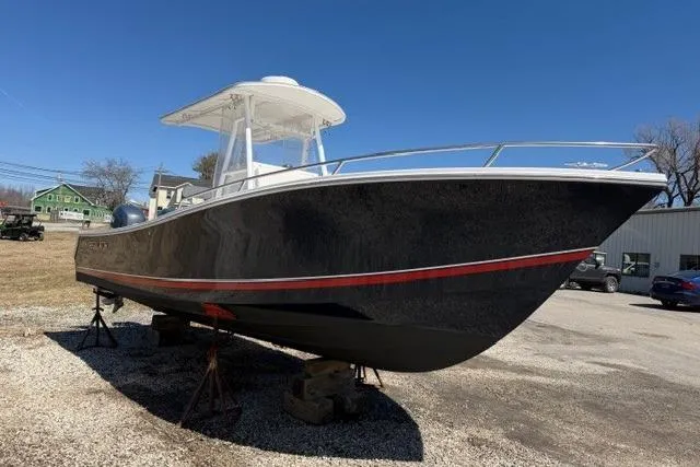 The Image of 2004 Regulator 24 Forward Seating boat on stands, black hull with red stripe, outdoor setting. - 0