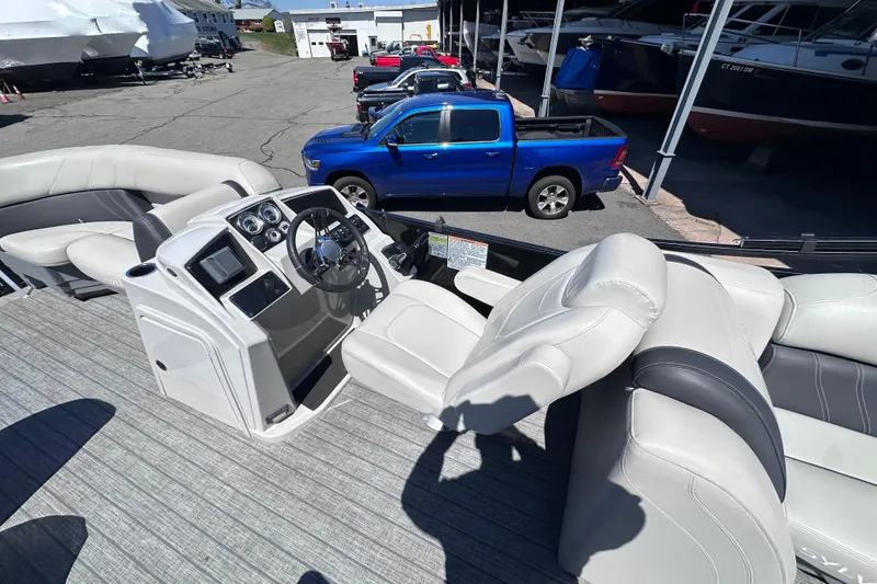 Slide: The Image of 2021 Sylvan Mirage X X3 boat interior with steering console and seating, parked near blue truck. - 12