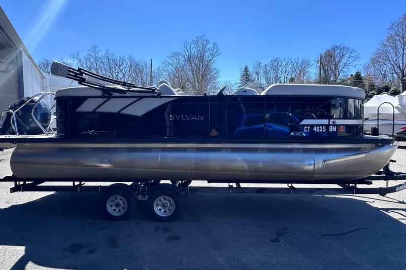 Slide: The Image of 2021 Sylvan Mirage X X3 pontoon boat on trailer, parked outdoors under clear blue sky. - 4