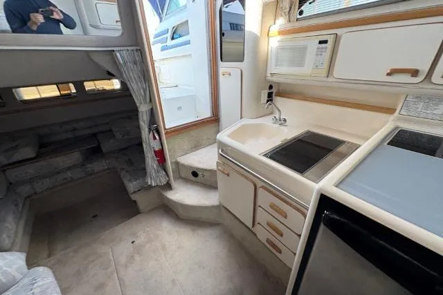 Slide: The Image of Interior of a 1993 Sea Ray Sundancer 330 yacht, featuring a compact kitchen and cozy seating area. - 90
