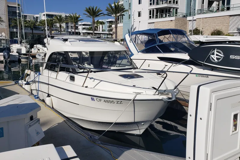 Slide: The Image of 2019 Beneteau Antares 23 docked at a marina with modern buildings in the background. - 2