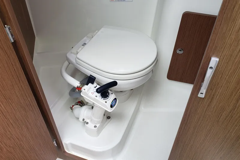 Slide: The Image of 2019 Beneteau Antares 23 boat bathroom with marine toilet and wooden accents. - 33