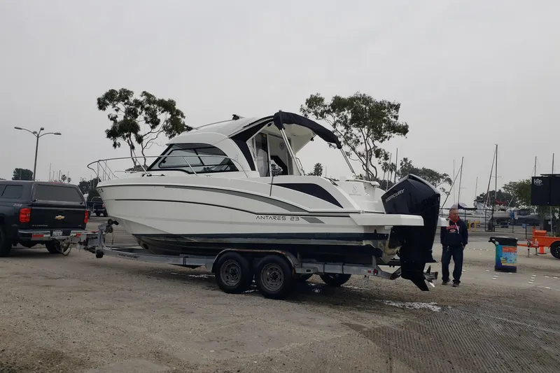 Slide: The Image of 2019 Beneteau Antares 23 boat on trailer, parked near marina with trees in background. - 57
