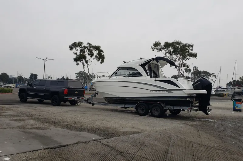 Slide: The Image of 2019 Beneteau Antares 23 boat on trailer, towed by a black truck in a marina. - 58
