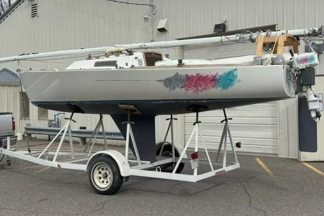 Slide: The Image of 1988 J Boats J/22 sailboat on trailer, showing colorful hull patches, parked outside a building. - 11
