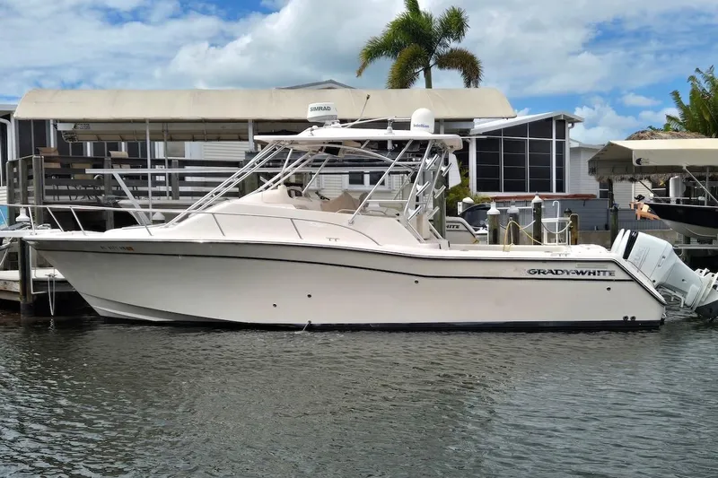 The Image of 2006 Grady-White Express 330 boat docked by waterfront homes under a cloudy sky. - 0