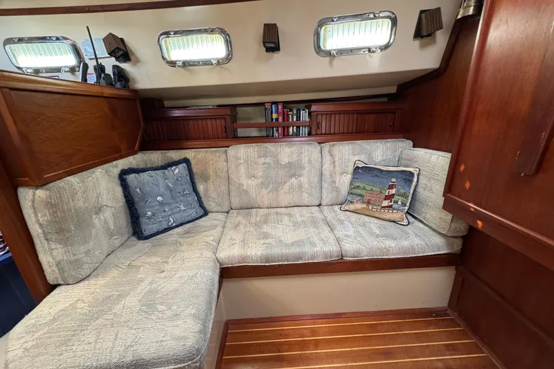 Slide: The Image of Cozy 1994 Island Packet 32 sailboat interior with cushioned seating and nautical-themed pillows. - 13