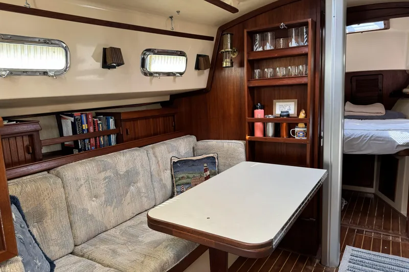 Slide: The Image of Cozy 1994 Island Packet 32 sailboat interior with dining area, bookshelves, and cabin view. - 19
