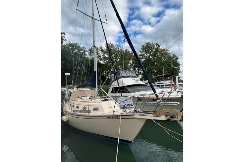 Slide: The Image of 1994 Island Packet 32 sailboat docked, surrounded by trees and other boats under a cloudy sky. - 9