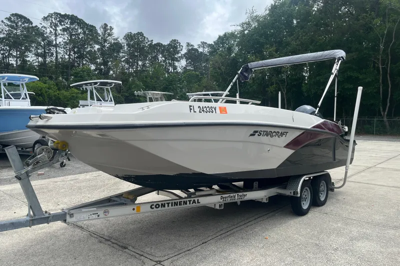 Slide: The Image of 2021 Starcraft SVX 211 OB boat on trailer, parked outdoors with trees in background. - 5