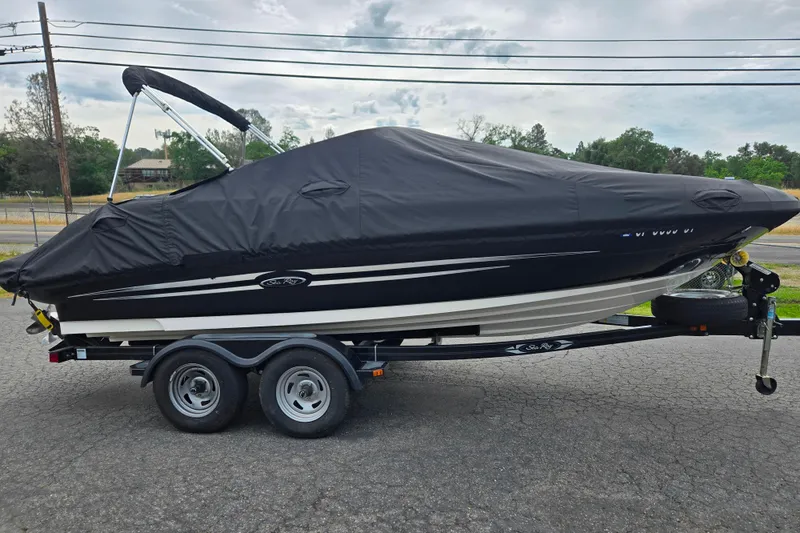 Slide: The Image of 2011 Sea Ray 200 Sundeck boat covered on a trailer, parked outdoors. - 22