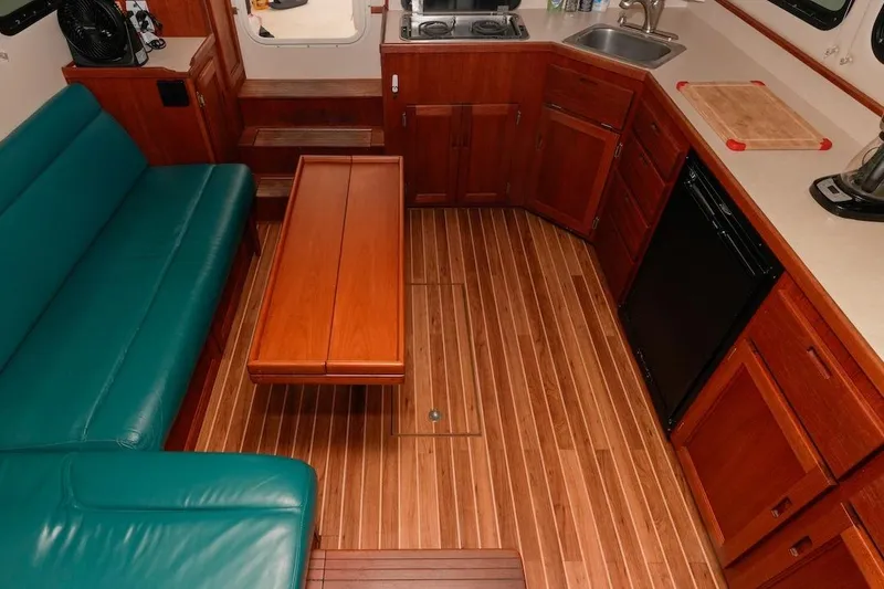 Slide: The Image of Interior of 2002 Nordic Tug 32 with wood flooring, teal seating, and compact kitchen area. - 8