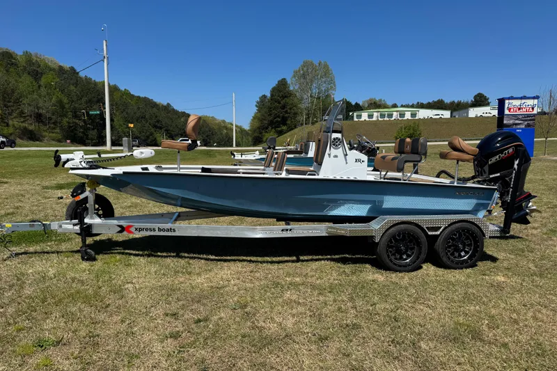 The Image of 2026 Xpress XR21 Bay boat on trailer, parked on grass under clear blue sky. - 0