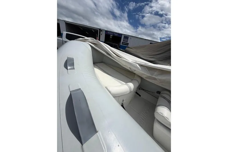Slide: The Image of 2010 Nautica RIB 14 inflatable boat with white interior, partially covered, under cloudy sky. - 6