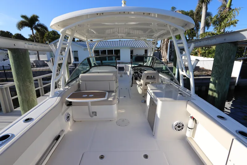 Slide: The Image of 2016 Boston Whaler 270 Vantage boat interior with seating and helm, docked near palm trees. - 13