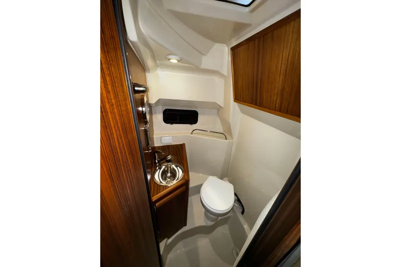 Slide: The Image of 2026 Ranger Tugs R-25 boat bathroom with sink, toilet, and wooden cabinetry. - 9
