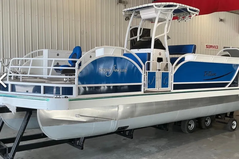 The Image of 2025 JC SportAngler 26TT HTH pontoon boat in showroom, featuring blue and white design. - 1
