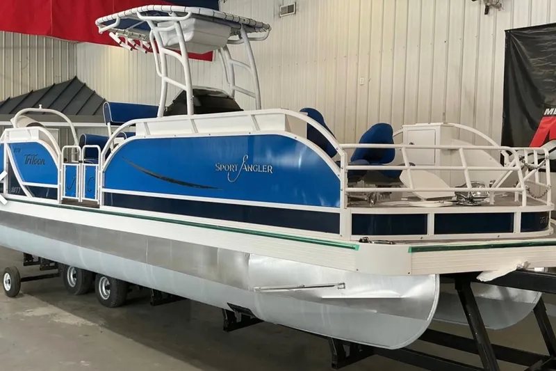 Slide: The Image of 2025 JC SportAngler 26TT HTH pontoon boat in showroom, featuring blue and white design. - 6