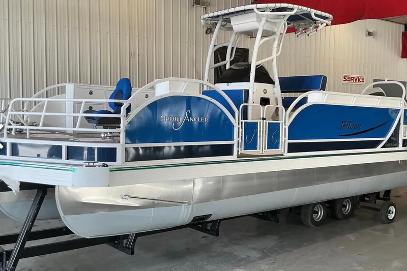 Slide: The Image of 2025 JC SportAngler 26TT HTH pontoon boat in a showroom, featuring blue and white design. - 7