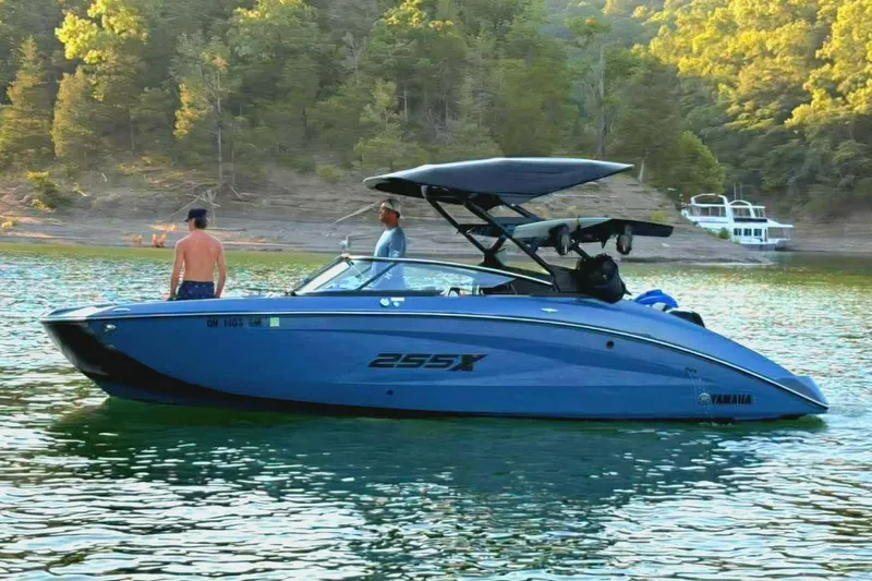 Slide: The Image of 2023 Yamaha Boats 255XD on a serene lake with lush forest backdrop. - 2