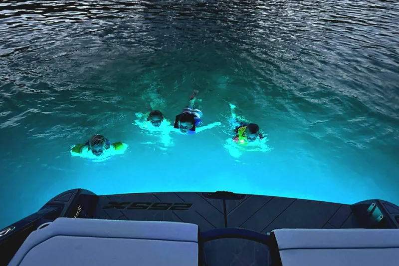 Slide: The Image of Four people swimming near a 2023 Yamaha Boats 255XD, illuminated by underwater lights. - 22