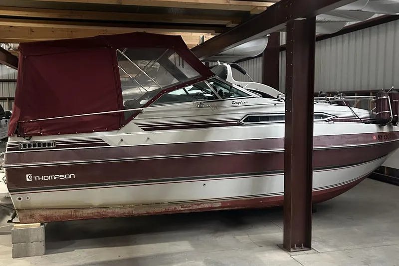The Image of 1990 Thompson 250 Daytona Mid Cabin boat stored indoors with maroon canopy. - 1