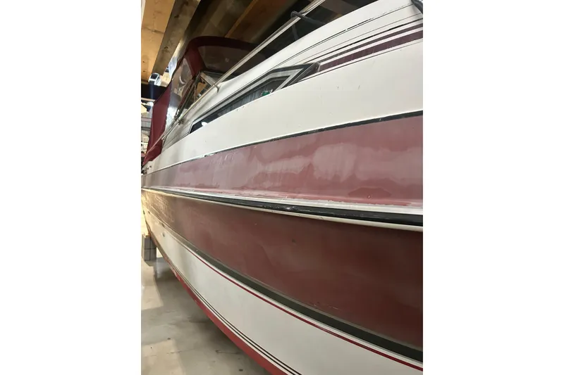 Slide: The Image of 1990 Thompson 250 Daytona Mid Cabin boat with red and white exterior in storage. - 11