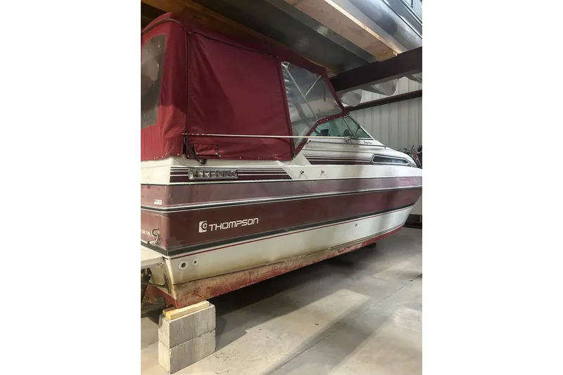 Slide: The Image of 1990 Thompson 250 Daytona Mid Cabin boat with maroon canopy in storage. - 4