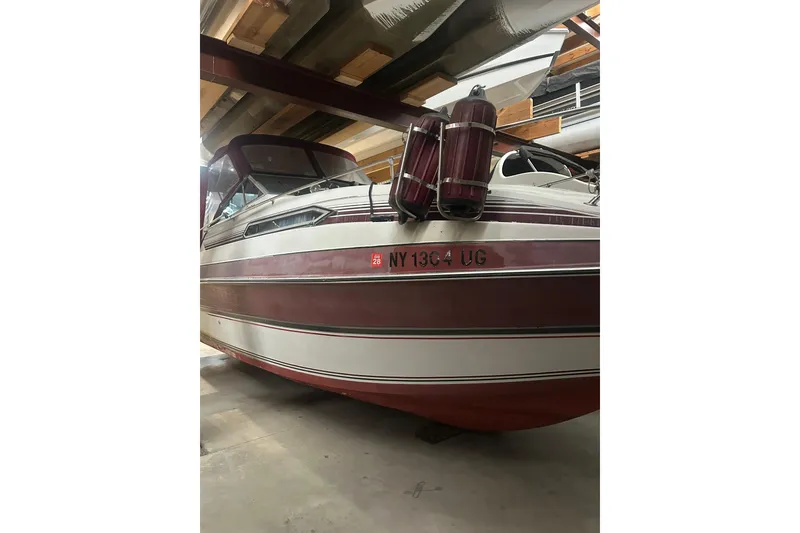 Slide: The Image of 1990 Thompson 250 Daytona Mid Cabin boat in storage, featuring maroon and white exterior. - 5