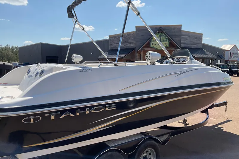 Slide: The Image of 2011 Tahoe 225 boat on trailer, parked outside a rustic building under a clear sky. - 1
