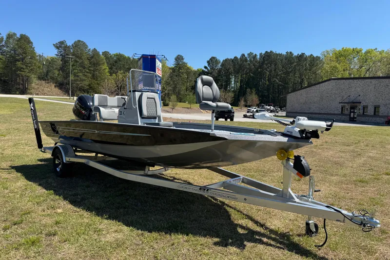 Slide: The Image of 2025 Xpress H20B Bay boat on trailer, parked on grass with trees in background. - 15