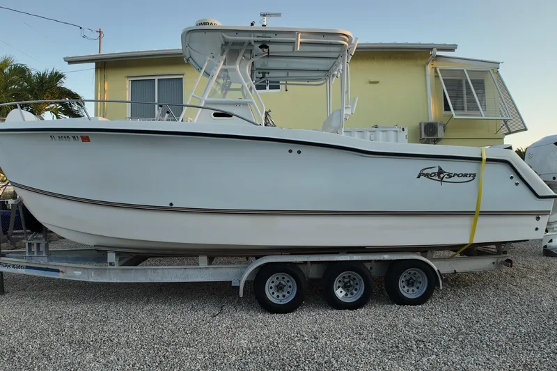 The Image of 2003 Pro Sports 2860 SC ProKat boat on trailer, parked near a yellow building. - 0
