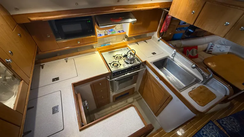 Slide: The Image of 2004 Catalina 470 yacht kitchen with stove, sink, microwave, and wooden cabinetry. - 13