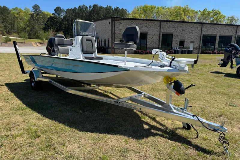Slide: The Image of 2026 Xpress H20B Bay boat on trailer, parked on grass, with building and trees in background. - 14