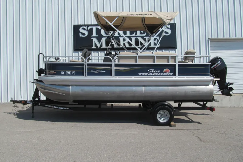 The Image of 2023 Sun Tracker Bass Buggy 18 DLX pontoon boat on trailer, parked outside marine store. - 1