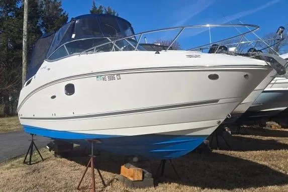 The Image of 2011 Sea Ray Sundancer 260 boat on stands, white hull with blue bottom, outdoors. - 0