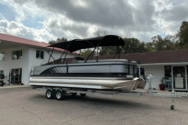 The Image of 2026 Qwest L-Class Splash Pad 24 pontoon boat on trailer, parked outside a building. - 0