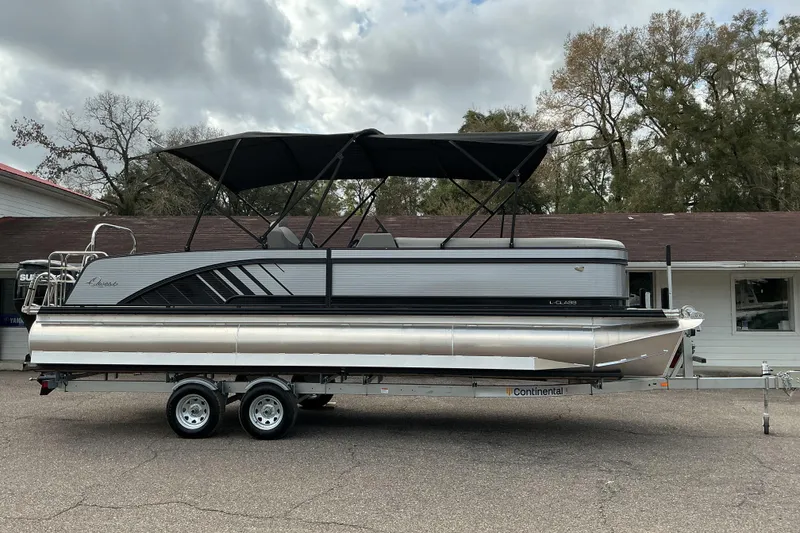 Slide: The Image of 2026 Qwest L-Class Splash Pad 24 pontoon boat on trailer, parked outdoors. - 1
