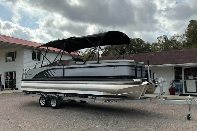 Slide: The Image of 2026 Qwest L-Class Splash Pad 24 pontoon boat on trailer, parked outside a building. - 3